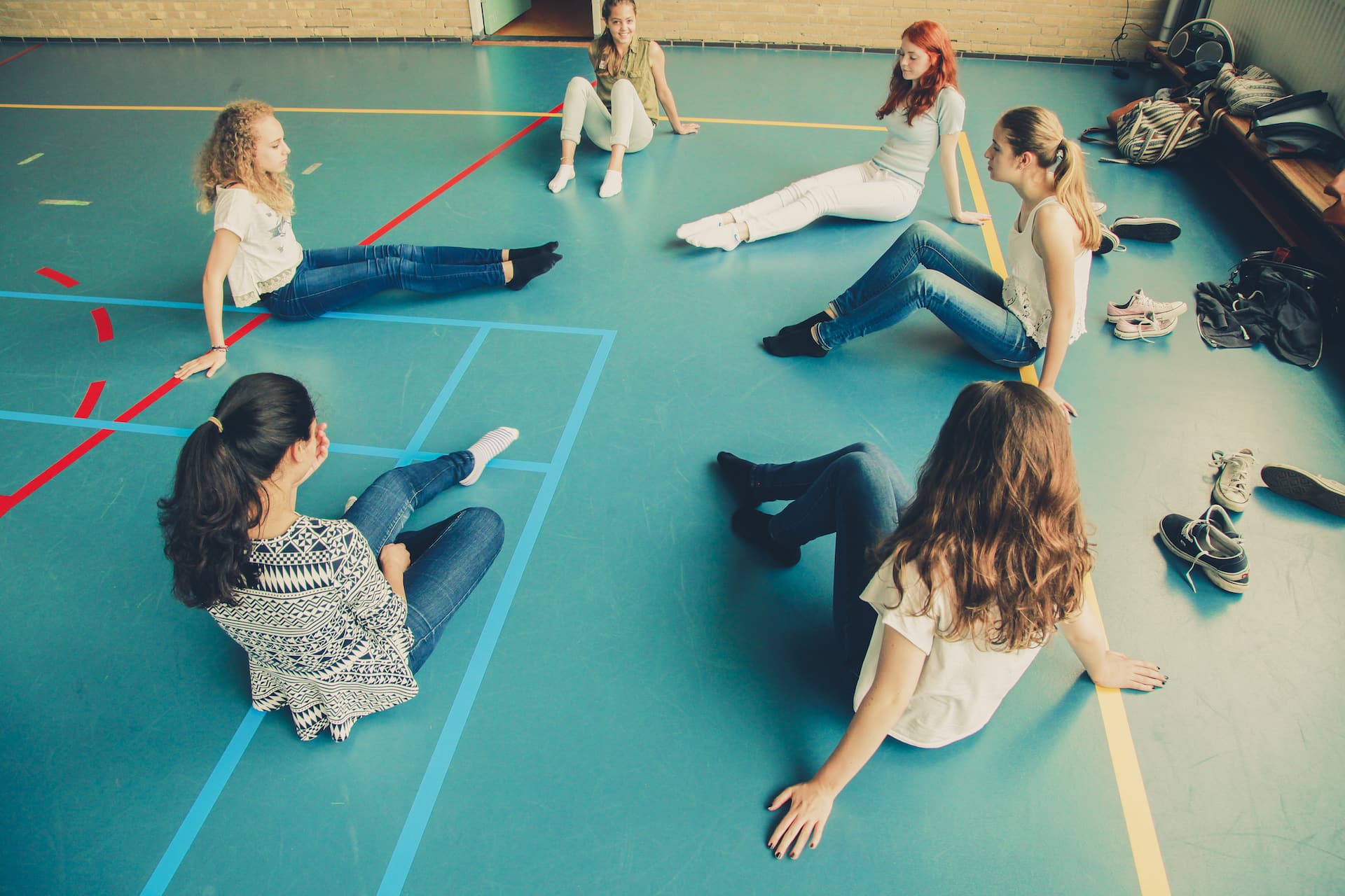 Leerlingen zitten in een kring op de gymzaalvloer tijdens een theaterworkshop